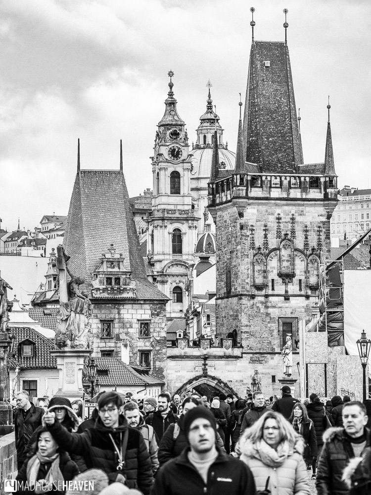 Charles Bridge packed with tourists tall and Gothic buildings rising out into the sky behind