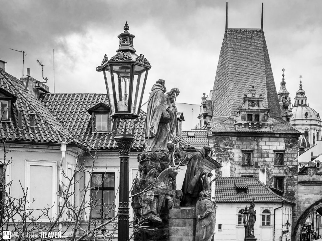 A view from Charles Bridge, with an old style lamp, a statue and Gothic roofs in the background